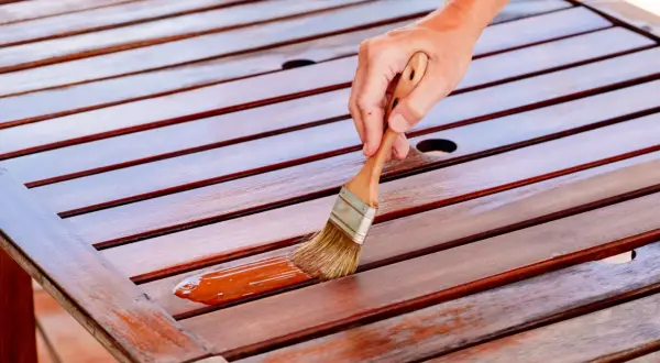 Mano aplicando barniz a una mesa de madera. Se puede barnizar sin tapaporos para un acabado rápido y protector.