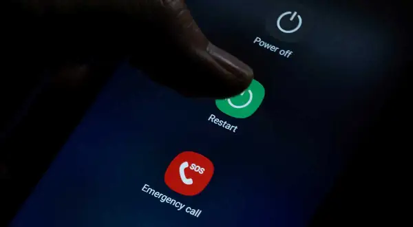 Palec naciska przycisk "Restart" na ekranie telefonu, co może pomóc, gdy zastanawiasz się, jak przywrócić poprzednie ustawienia telefonu.