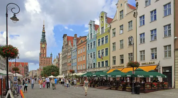 Färgglada hus längs en livlig gågata på långa marknaden Gdansk. Folk promenerar och njuter av solen vid uteserveringar.