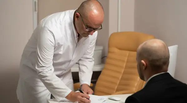 Lekarz w białym kitlu pochyla się nad dokumentami, omawiając z pacjentem wyniki badań, które mogą wskazywać na raka in situ sutka.