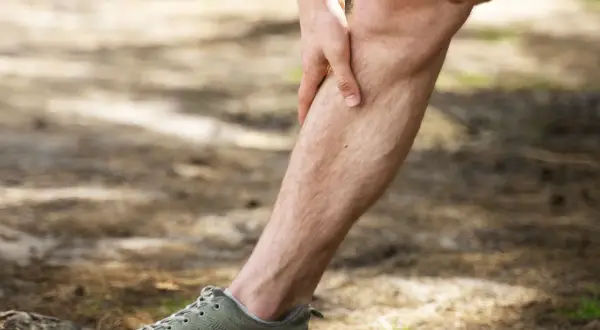 Uomo con mano sulla tibia, avvertendo dolore tibiale anteriore a riposo. Scarpa da ginnastica verde in primo piano.