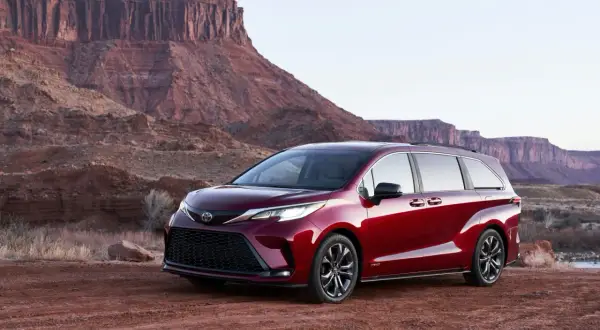 Czerwony minivan Toyota Sienna Hybrid na tle pustynnego krajobrazu z klifami.