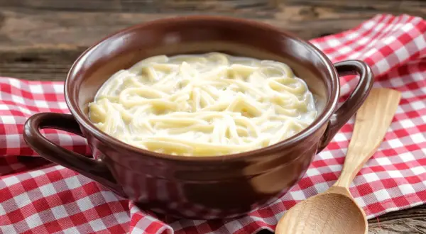 Eine Schüssel mit milch nudeln, serviert auf kariertem Stoff. Ein Holzlöffel liegt daneben.