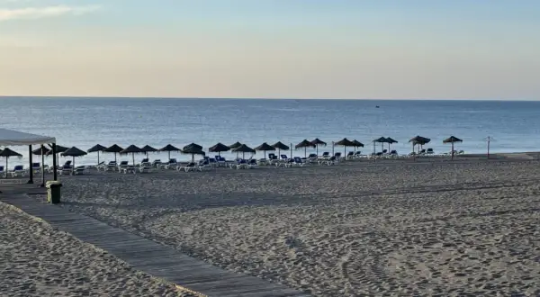 Playa marina de la torre con arena fina y tumbonas bajo sombrillas. El mar tranquilo se extiende hasta el horizonte.