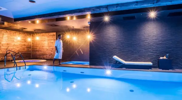 Mężczyzna w szlafroku spaceruje po luksusowej strefie dla dorosłych z basenem i jacuzzi.