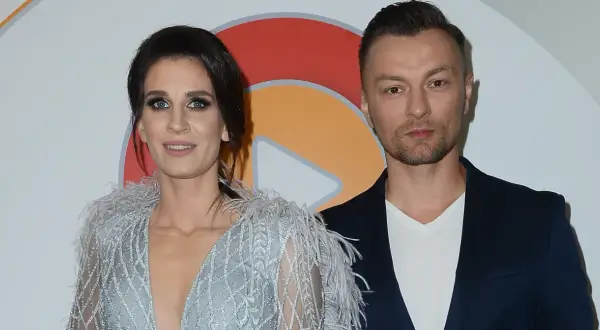 Sylwia Grzeszczak i Liber pozują do zdjęcia. Ona w błyszczącej sukni z piórami, on w granatowej marynarce.