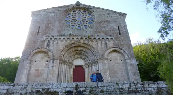 Dos personas posan frente a la fachada románica de Santo Estevo de Ribas de Miño, con su rosetón y portal detallados.