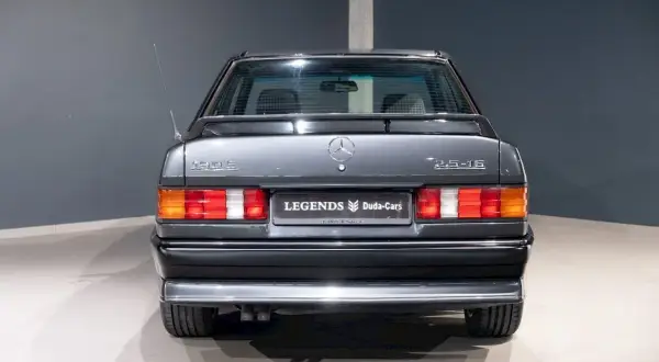 Tył szarego Mercedesa 190 2.5-16 z lat 80. z antenką i emblematami.