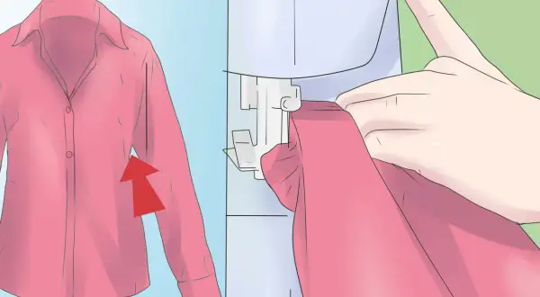 Mani che guidano una maglietta rosa sotto una macchina da cucire, con un'immagine ingrandita della maglietta che mostra una freccia rossa. Impara come restringere una maglietta.