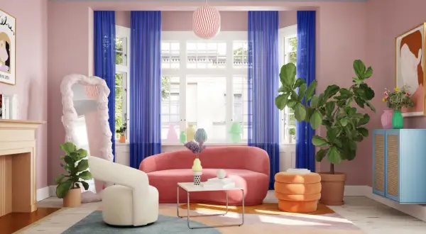 Ein rosa Sofa wird von kräftigen blauen Vorhängen und einem bunten Teppich umrahmt. Welche Farbe passt zu rosa? Hier: Blau, Orange und Grün!