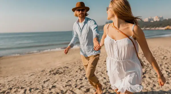 Szczęśliwa para biegnie plażą, trzymając się za ręce. Słońce, morze i piaszczysta promenada nad morzem tworzą idealne tło dla ich wakacyjnej przygody.
