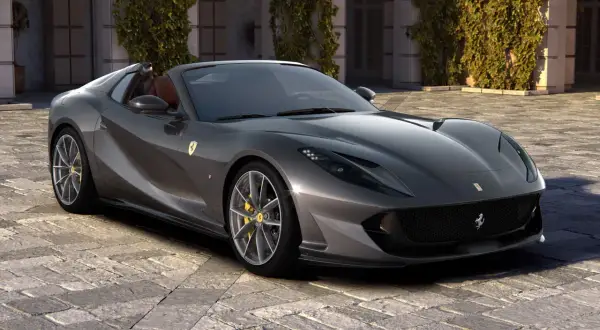 Szary kabriolet Ferrari 812 GTS z żółtymi zaciskami hamulcowymi stoi na brukowanym dziedzińcu przed budynkiem porośniętym bluszczem.