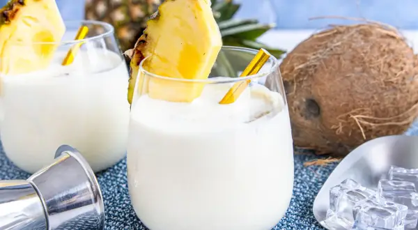 Zwei cremige Kokos-Ananas-Cocktails, garniert mit Ananasstücken, versprechen einen tropischen Genuss. Ein Hauch von "coconut kiss" für heiße Tage.
