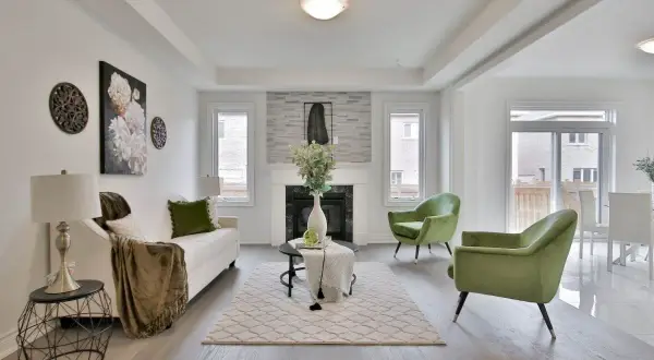 Salon moderne avec canapé blanc, fauteuils verts et cheminée. Le tapis et les coussins apportent une touche de blanc cassé.