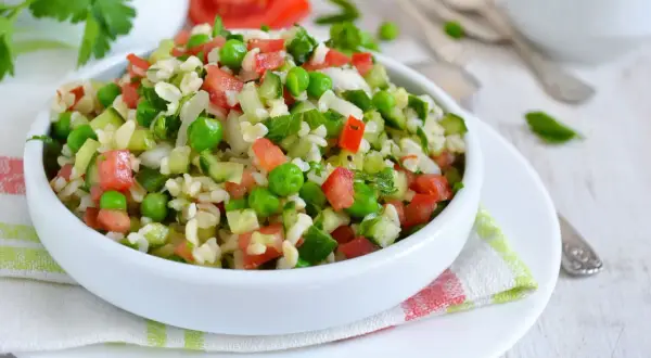 Orzeźwiająca sałatka z kaszą bulgur, pomidorami, ogórkiem i zielonym groszkiem, doprawiona fetą.