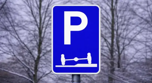 Blå parkeringsskylt med vitt P och en bild av en axel med hjul på en ramp. Förståelse av parkeringsskyltar är viktigt för att veta var man får parkera.