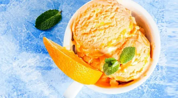 Erfrischendes orangen sorbet in einer Schale, garniert mit Minze und einer Orangenspalte auf blauem Untergrund.
