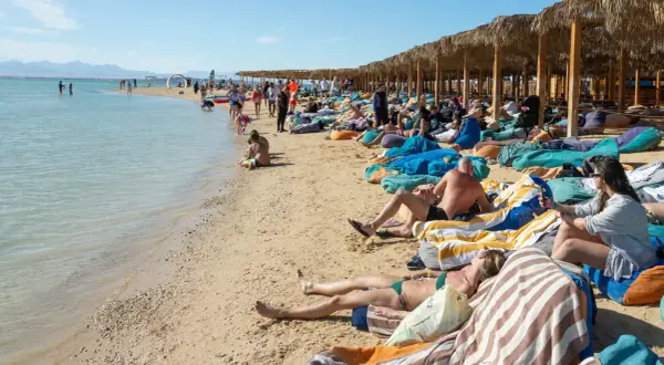 Ludzie odpoczywają na plaży w Egipcie. Idealna pogoda w Egipcie w grudniu sprzyja relaksowi na leżakach pod palmowymi zacienionymi wiatami.