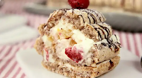 En läcker budapestbakelse med vispgrädde, frukt och chokladdrizzle, toppad med ett hallon.