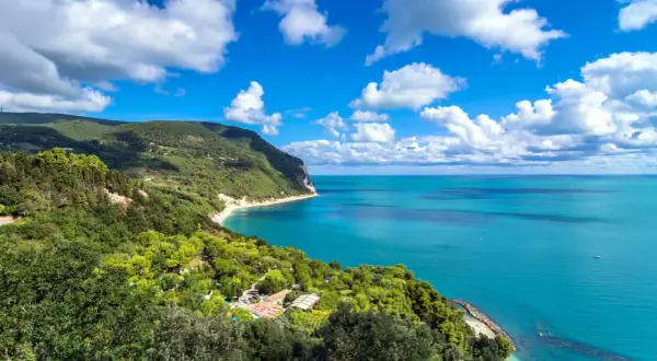 Vista mozzafiato dal belvedere Monte Conero: mare azzurro, costa verdeggiante e nuvole bianche nel cielo.