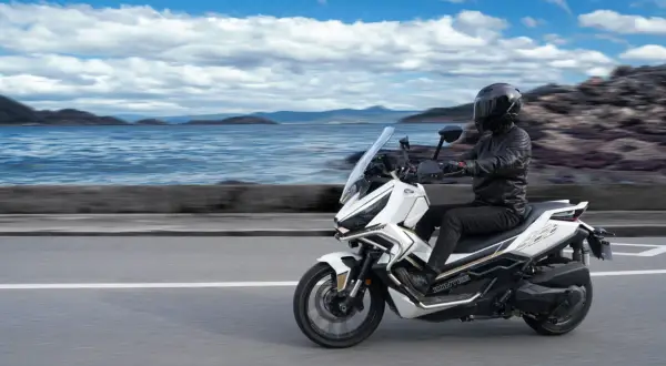 Conductor en moto Zontes 368G blanca, con paisaje marino y montañas. ¡Las opiniones sobre esta moto son excelentes!