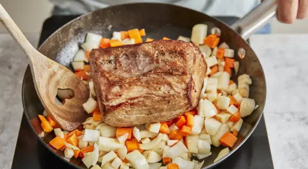 Ein gebratener Rinderbraten ruht auf gewürfeltem Wurzelgemüse in einer Pfanne. Perfekt für ein herzhaftes rinderbraten rezept.