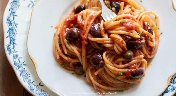 Un piatto invitante di spaghetti alla puttanesca, con olive nere, capperi e un sugo rosso vivace, pronto per essere gustato.