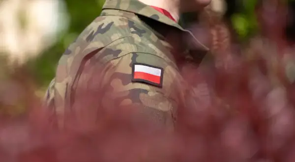 Żołnierz w mundurze z polską flagą. W tle zamazane czerwone liście i zieleń. Choroby dyskwalifikujące ze służby wojskowej mogą wpłynąć na możliwość noszenia takiego munduru.