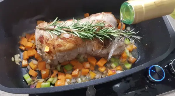 Arrosto di vitello in pentola con verdure e rosmarino, mentre viene sfumato con vino bianco.