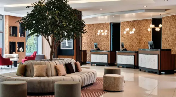 Eleganckie lobby hotelu Radisson Blu Hotel Krakow z okrągłą sofą, drzewem i recepcją z drewnianą ścianą.