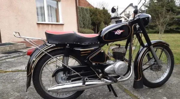 Czarny motocykl WSK z czerwoną kanapą i złotymi ozdobami, stojący na podjeździe.