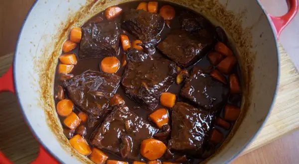 Sabroso plato típico de Francia: ternera estofada en salsa oscura con zanahorias y champiñones en una olla roja.