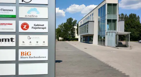 Tablica z nazwami firm, w tym "BiG Biuro Rachunkowe", przed nowoczesnym budynkiem biurowym.