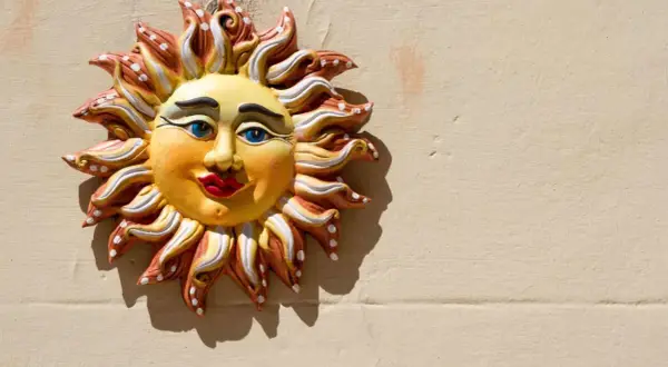 Sole decorativo in ceramica, un esempio di artigianato italiano, con volto sorridente e raggi colorati su muro beige.