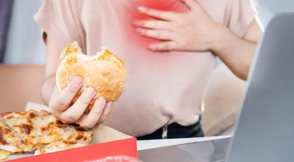 Osoba z bólem w klatce piersiowej trzyma gryzionego burgera. Obok pizza. Zastanawia się, co jeść na zgagę.