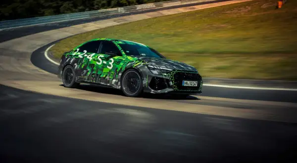 Rs3 Audi w zielono-czarnej kamuflażowej okleinie pędzi po torze wyścigowym.