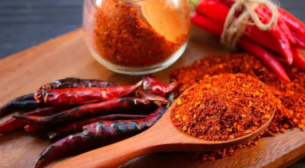 Ein Holzlöffel voller Cayennepfeffer-Flocken zeigt, woraus Cayennepfeffer hergestellt wird: getrocknete Chilischoten.