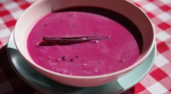 Aksamitna zupa jagodowa z laską wanilii, podana w miseczce na kraciastym obrusie.