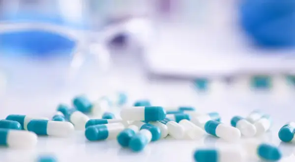 Kapsułki z antybiotykami w kolorze białym i turkusowym leżą na białej powierzchni.