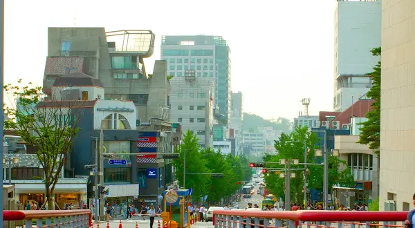 Tętniąca życiem ulica w **Hongdae**, pełna ludzi, sklepów i nowoczesnej architektury, z widokiem na wzgórza w tle.