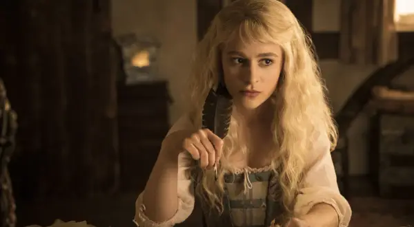 Sophia Anne Caruso sitzt nachdenklich am Schreibtisch und hält eine Feder.