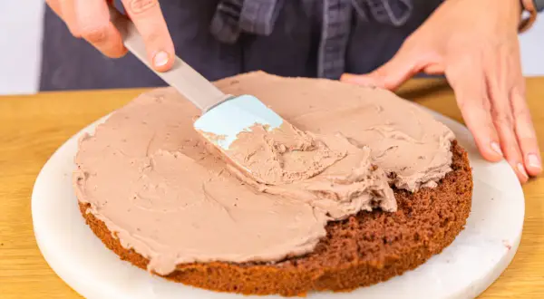 Eine Schokoladentorte wird mit einer cremigen Füllung bestrichen, die an Kinder Bueno Torte erinnert.