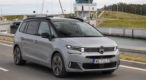 Srebrny Citroen Picasso jedzie drogą obok kanału. W tle widoczna wieża kontrolna i podniesiony most.