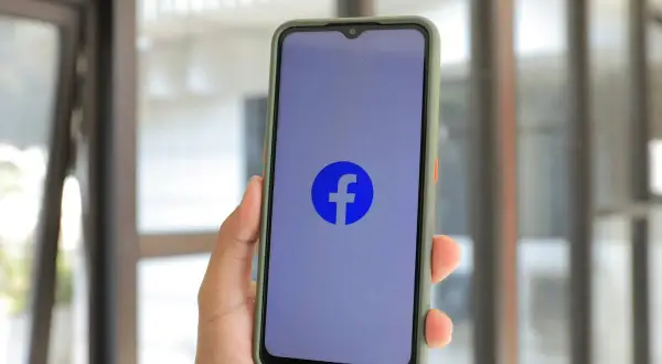 Dłoń trzyma smartfon z logo Facebooka. Chcesz wiedzieć, jak wyłączyć urodziny na FB?