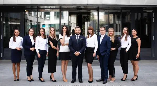 Grupa profesjonalistów w eleganckich strojach stoi przed nowoczesnym budynkiem.