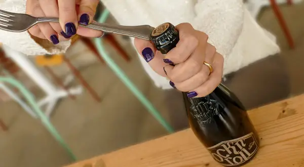 Mani con smalto viola usano una forchetta per mostrare come aprire una birra.