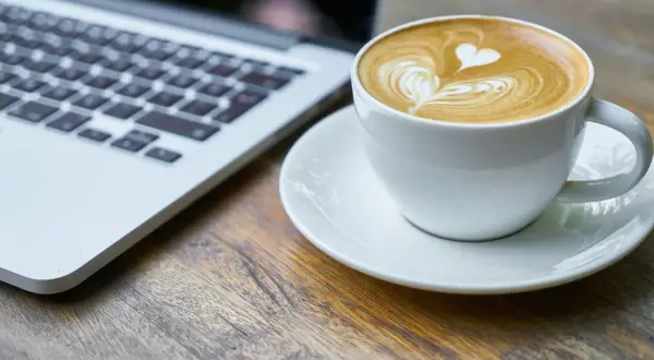 Kawa latte z sercem na piance obok laptopa. Idealny moment na relaks i picie kawy po operacji zaćmy.