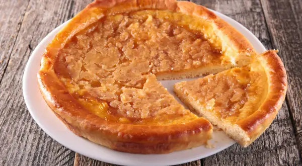 Une tarte au sucre dorée, avec une tranche coupée, sur une assiette blanche posée sur un fond en bois rustique.