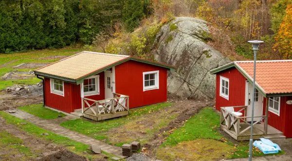 Dos casitas rojas de madera, ideales para un terreno. Rodeadas de naturaleza y una gran roca.