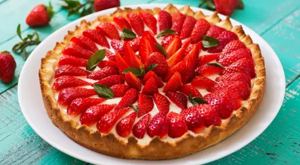 Pyszna tarta z owocami, pełna świeżych, czerwonych truskawek i listków mięty, na chrupiącym spodzie.